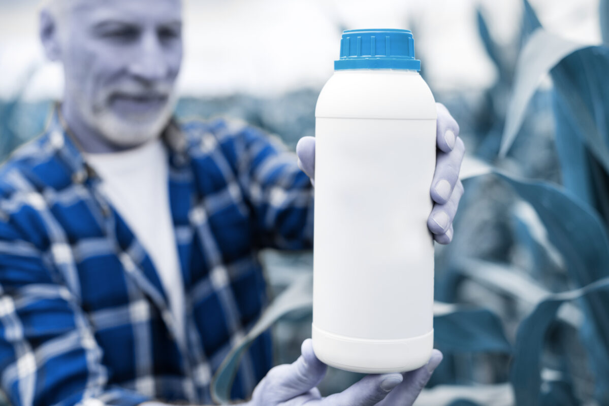 Grower holding a white fertilizer bottle in a field